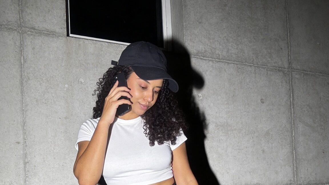 Daisy wearing a cap and holding a phone outdoors.